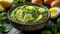 Traditional spinach and egg curry served in rustic ceramic bowl, garnished with halved boiled eggs and fresh herbs on dark stone surface.