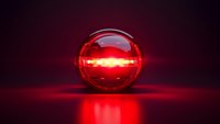 Glowing red glass sphere with mysterious light emanating from within, casting dramatic reflections on dark surface against black background with atmospheric lighting.