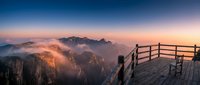 Wooden viewing platform overlooks misty mountain peaks at sunrise, with dramatic cliffs and valleys shrouded in fog. Ideal for travel, nature, and landscape design projects.