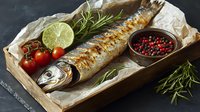 Grilled mackerel on parchment paper with fresh lime, cherry tomatoes, rosemary sprigs and pink peppercorns in wooden bowl. Dark moody food photography.