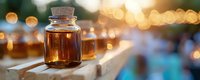 Glass bottle with cork containing amber liquid on wooden surface against blurred bokeh lights background, creating warm atmospheric mood at dusk.