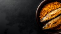 Two fresh fish seasoned with vibrant orange spice blend in dark bowl on textured black surface for culinary cooking and food preparation.