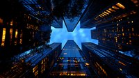 Modern skyscrapers photographed from below against dark blue evening sky, creating dramatic upward perspective with glowing office windows and architectural lines.
