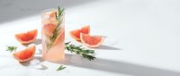 Refreshing grapefruit cocktail with rosemary garnish and ice cubes on white background. Summer citrus drink with fresh fruit slices for beverage menu design.