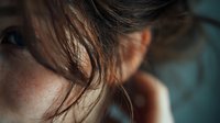 Young woman with freckled skin and brown hair in soft natural light, intimate portrait showing delicate facial features and gentle expression.