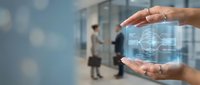 Hands holding transparent digital cube with holographic brain scan interface in modern office environment with blurred business professionals.