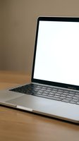 Modern silver laptop computer with blank white screen open on wooden desk surface against neutral beige wall background for business presentations and mockups.