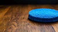 Bright blue circular cleaning brush on wooden surface with dramatic lighting and shallow depth of field, highlighting texture and bristles.