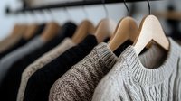 Cozy knitted sweaters in neutral colors hanging on wooden hangers in closet, selective focus on beige and gray wool garments. Fashion retail display.