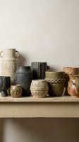 Collection of handmade ceramic vessels with geometric patterns displayed on wooden shelf. Includes cream, black, green and terracotta pots with carved details for home decor and interior styling.