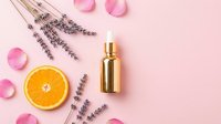 Luxury gold dropper bottle with lavender sprigs, orange slice, and rose petals on pink background, skincare and beauty product concept.