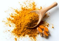 Vibrant turmeric powder spilling from wooden spoon with fresh root pieces, showcasing golden yellow spice for cooking and health benefits.