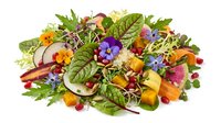 Fresh gourmet salad with edible flowers, mixed greens, roasted squash, pomegranate seeds, and microgreens, isolated on white background.