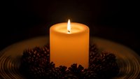 Warm glowing candle surrounded by coffee beans on wooden surface creates cozy atmospheric lighting for relaxation and aromatherapy concepts.
