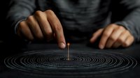 Burning incense stick creates circular smoke pattern on dark surface as Asian male hands hold it, dramatic moody lighting creates zen atmosphere for meditation practice.