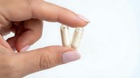 Hand holding two white capsules or pills between fingers on clean white background for healthcare and medicine concepts.