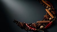 Aromatic spices cinnamon sticks star anise nutmeg chili peppers arranged in circular frame on dark background for culinary cooking baking holiday recipes.