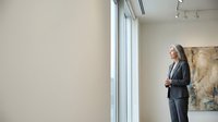 Professional businesswoman in elegant suit standing by large windows in modern office space looking thoughtful and confident during workday.