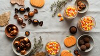 Autumn flat lay with candy corn, chocolate truffles, pumpkin decorations and herbs on marble surface for seasonal celebrations and Halloween treats.