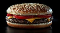 Classic cheeseburger with beef patty, melted cheese, tomato and sesame seed bun on dark background, dramatic lighting creates appetizing food photography.