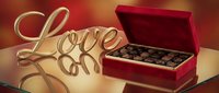 Gold Love sign beside open red velvet box of assorted chocolates on reflective surface, warm romantic bokeh background for Valentine's Day.