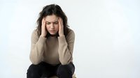 Young woman experiencing severe headache holding head in hands showing stress and mental health struggles on white background.