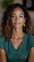 Young mixed race woman with curly hair wearing green v-neck top and gold earrings smiling warmly at camera. Natural makeup and glowing skin create welcoming professional portrait.