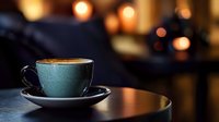 Teal ceramic cup filled with hot coffee on saucer, positioned on wooden table with warm bokeh lights in blurred background, suitable for cafe, beverage, and lifestyle designs.