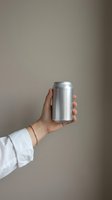 Hand holding blank aluminum can mockup against neutral beige background for branding and packaging design projects.