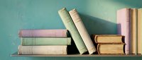 Stack of vintage books with worn spines in pastel colors arranged on wooden shelf against turquoise wall for literary and educational design projects.