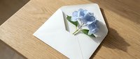 White envelope with blue hydrangea flowers on wooden table for wedding invitations, greeting cards, and romantic correspondence designs.
