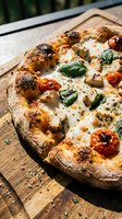 Freshly baked pizza with charred crust, melted mozzarella cheese, roasted tomatoes, and fresh basil leaves on wooden serving board outdoors.