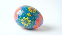 Colorful painted Easter egg with floral pattern featuring yellow flowers and decorative swirls on blue and coral background isolated on white.
