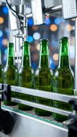 Green beer bottles with condensation on conveyor belt in modern brewery facility with industrial lighting and blurred background.