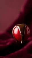 Heart-shaped chocolate candy with glossy coating and red center on burgundy silk fabric background for Valentine's Day romantic dessert concepts.