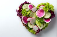 Fresh vegetable salad arranged in heart shape with cucumber, radish and mixed greens on white background for healthy eating and diet concepts.