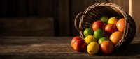 Fresh colorful fruits spilling from wicker basket on rustic wooden table with warm natural lighting for healthy eating and harvest concepts.