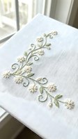 Delicate hand embroidered floral vine with white daisies and green leaves on natural linen fabric, traditional needlework craft for home decor and textile art.