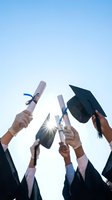 Graduates celebrating achievement holding diplomas and mortarboard caps against bright blue sky with sunburst for education success concepts.