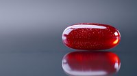 Red translucent pill capsule with sparkles inside on reflective dark surface with mirror effect, pharmaceutical and medical concept background.