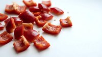 Fresh red bell pepper pieces chopped and scattered on white background, isolated vegetable ingredient ready for cooking and culinary design projects.
