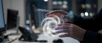 Hands holding a glowing holographic anomaly detection sphere in a dark office, representing AI cybersecurity and data analysis technology.