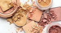 Crushed makeup powder cosmetics in warm nude and pink tones scattered on white background. Beauty products for professional makeup artists and skincare routines.