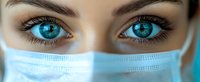 Close up view of bright blue eyes with long eyelashes and expressive eyebrows above protective medical face mask, representing healthcare and safety during pandemic.