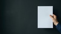 Hand holding blank white paper sheet against dark background, suitable for mockups, presentations, advertising campaigns, and design templates.