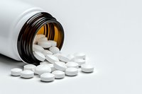 White pharmaceutical pills spilling from brown prescription bottle on neutral background, dramatic lighting highlights medical concept for healthcare industry.