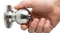 Hand holding modern stainless steel door knob handle on white background, home security hardware component for interior design and renovation projects.
