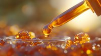 Amber liquid drops falling from dropper onto glass surface with golden bokeh background, creating spherical formations in macro photography.