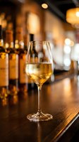 Glass of white wine on wooden bar counter with blurred bottles and warm lighting in upscale restaurant or pub atmosphere for hospitality industry.