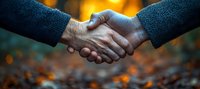 Close-up of firm business handshake between two people wearing dark suits against blurred warm bokeh background, symbolizing trust and partnership agreement.
